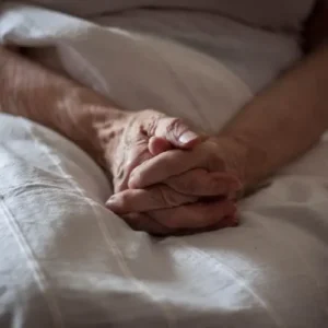 A nursing home resident holding her hands while sitting in a bed